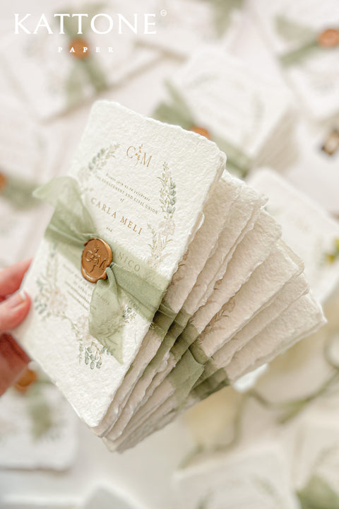 These handmade paper engagement invitations are a true keepsake for life’s most meaningful moments. Printed on luxury deckled-edge cotton paper, each piece showcases the soft texture and organic edges that make handmade paper so timeless and special. Adorned with watercolor botanical illustrations in gentle sage and blush tones, the design radiates natural elegance. The suite is finished with a translucent green silk ribbon and wax seal featuring the couple’s monogram.