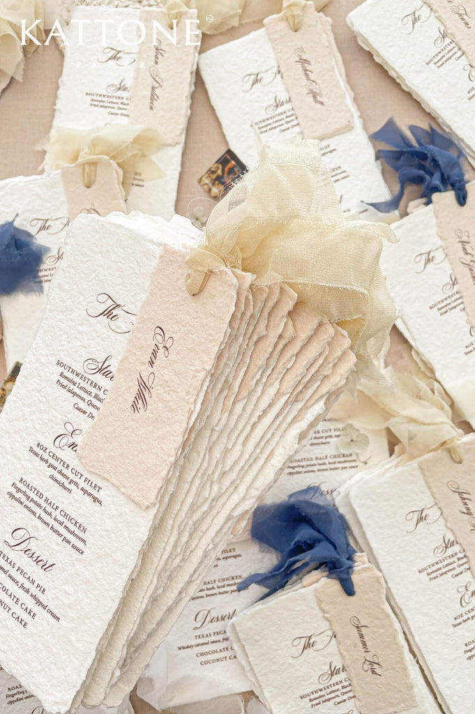Personalized handmade paper guest name tags layered over wedding menus create an elevated and thoughtful seating presentation.
