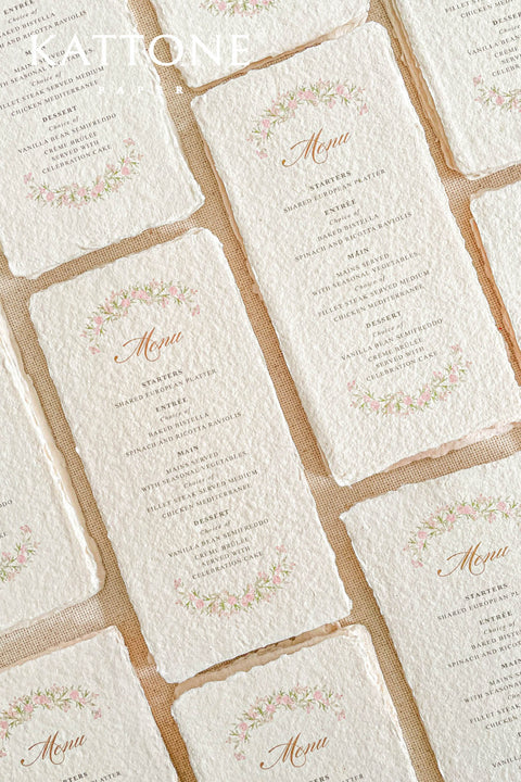 These handmade paper wedding menus radiate romantic charm and timeless artistry. Crafted from luxurious 100% cotton rag paper, each menu features natural deckled edges and a soft, tactile texture that instantly evokes the feeling of fine art stationery. The design is adorned with a delicate watercolor floral wreath in soft blush and green tones, surrounding elegant calligraphy-style lettering - creating a harmonious blend of refinement and nature-inspired beauty.