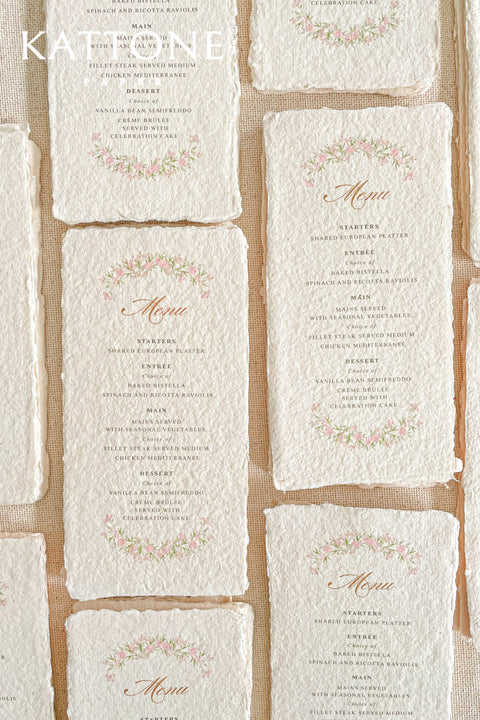 These handmade paper wedding menus radiate romantic charm and timeless artistry. Crafted from luxurious 100% cotton rag paper, each menu features natural deckled edges and a soft, tactile texture that instantly evokes the feeling of fine art stationery. The design is adorned with a delicate watercolor floral wreath in soft blush and green tones, surrounding elegant calligraphy-style lettering - creating a harmonious blend of refinement and nature-inspired beauty.