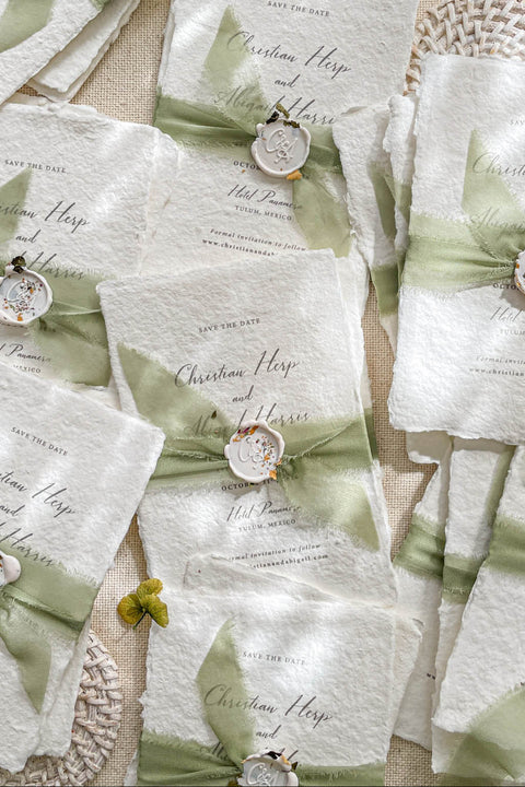 Capture the romance of your wedding day with these exquisite handmade paper Save the Date cards, elegantly wrapped in sage green silk ribbon and adorned with a pressed floral wax seal. Printed on 100% cotton paper with naturally deckled edges, each card embodies timeless craftsmanship and fine art design - a beautiful prelude to your celebration.
