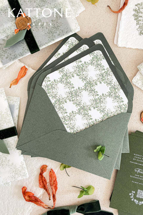 Soft green wedding envelopes with watercolor floral envelope liners styled on linen with botanical accents and fine art stationery details.