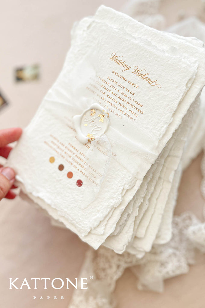 Close up of handmade cotton paper invitation highlighting textured deckled edges, elegant gold typography and soft artisanal paper surface.