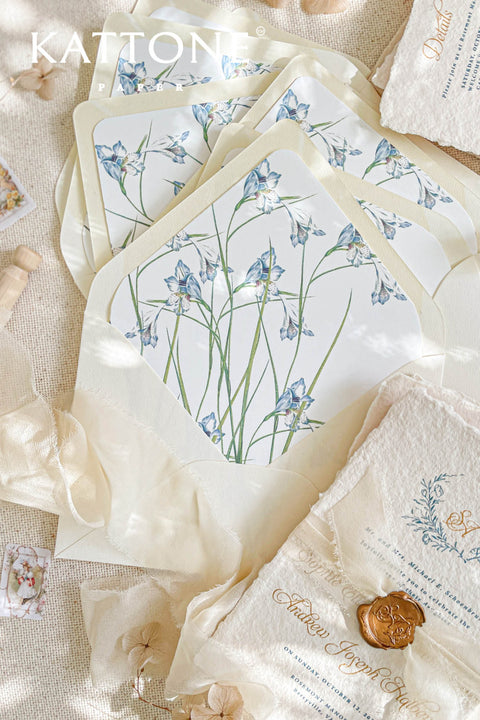 Ivory wedding envelopes with watercolor floral envelope liners styled with silk ribbon, handmade paper, and fine art wedding stationery details.