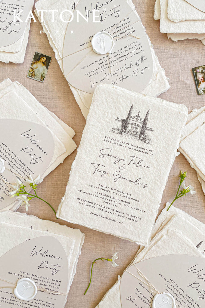 Flat lay of luxury wedding stationery including handmade paper invitations, welcome cards, envelopes, and venue illustration artwork.