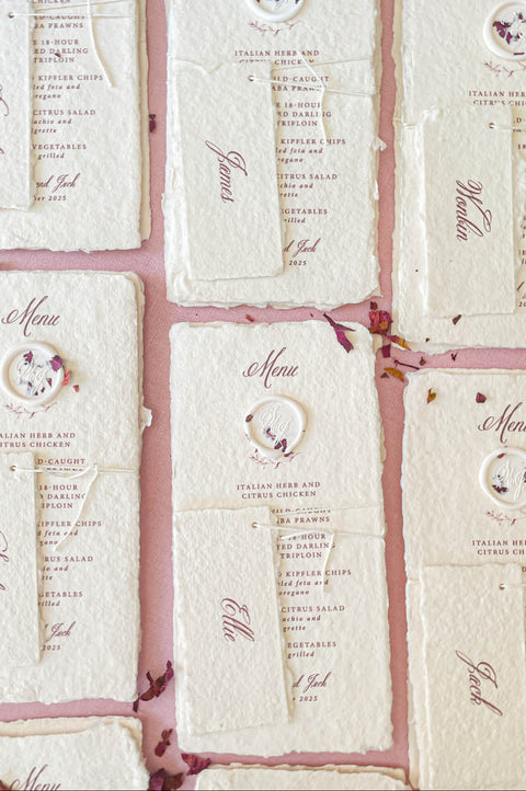 Luxury wedding menu on handmade paper featuring wax seal accent and soft neutral color palette.