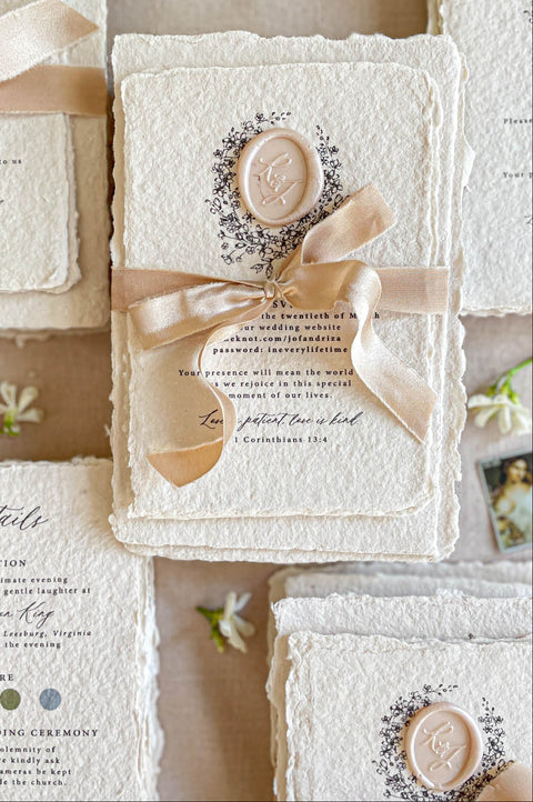Wedding invitations finished with silk ribbon and custom wax seal on textured handmade paper.