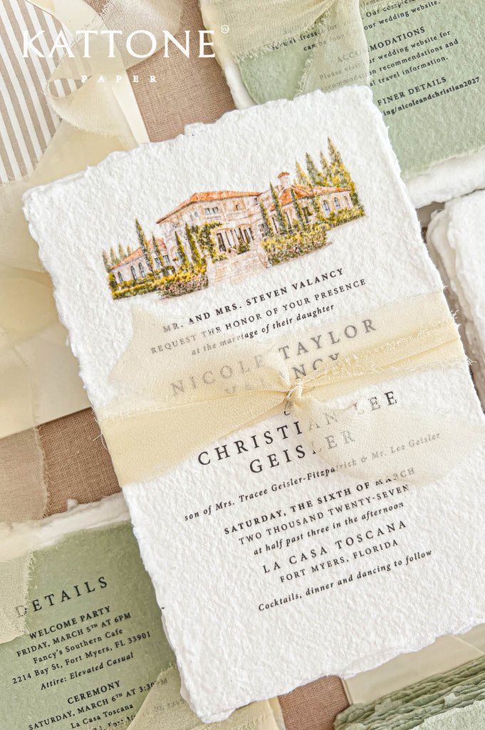 Close-up of an ivory handmade paper wedding invitation featuring a custom watercolor illustration of a Tuscan-inspired villa with terracotta roofs, cypress trees and landscaped gardens, finished with a sheer ivory ribbon and elegant black typography. Sage green details cards appear in the background.