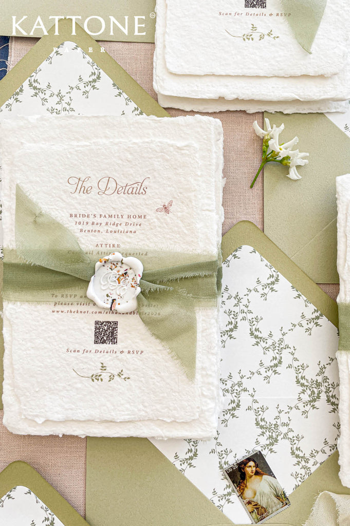 Close up of textured handmade cotton paper wedding invitation featuring botanical monogram wreath and elegant serif typography.
