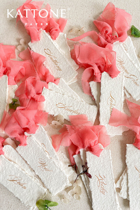 Bring a lively, romantic touch to your event with our handmade paper place cards, featuring natural deckled edges, vibrant coral chiffon ribbon, and elegant gold calligraphy. Crafted individually for a fine-art, textural finish, these name cards elevate any wedding tablescape with their vivid color and artisanal charm. Perfect for modern, garden, summer, and destination weddings.