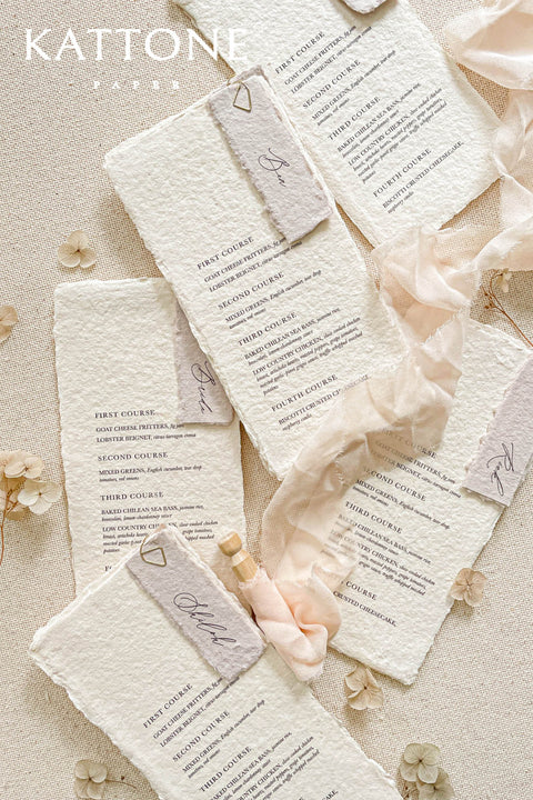 These handmade paper wedding menus embody the essence of soft romance and fine art elegance. Crafted from luxurious 100% cotton rag paper, each piece features delicate deckled edges and a naturally soft texture that enhances its artisanal appeal. The minimalist typography is printed in rich, elegant ink, paired with a vellum-inspired place card and silky blush ribbon, creating a layered and ethereal look perfect for modern romantic tablescapes.