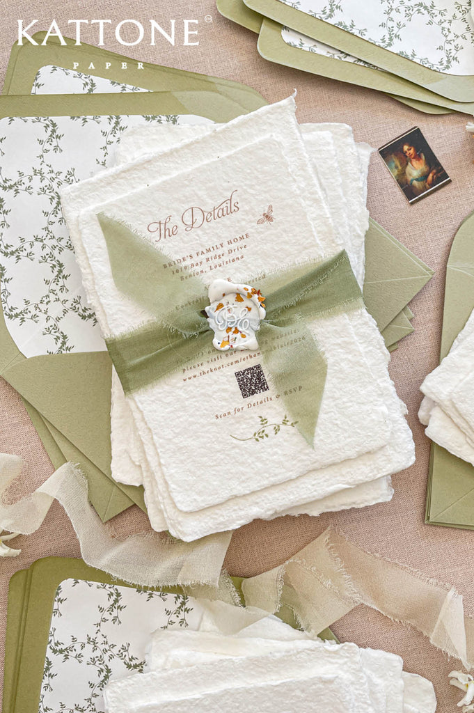 Close up of textured handmade cotton paper wedding invitation featuring botanical monogram wreath and elegant serif typography.