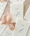 Luxury handmade paper reserved seat cards and table numbers featuring deckled edge cotton paper, elegant blue typography, and blush chiffon ribbon styling.