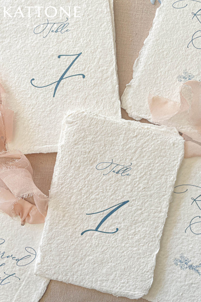 Elegant handmade paper reserved seat card with deckled edges featuring refined blue typography and floral detailing.