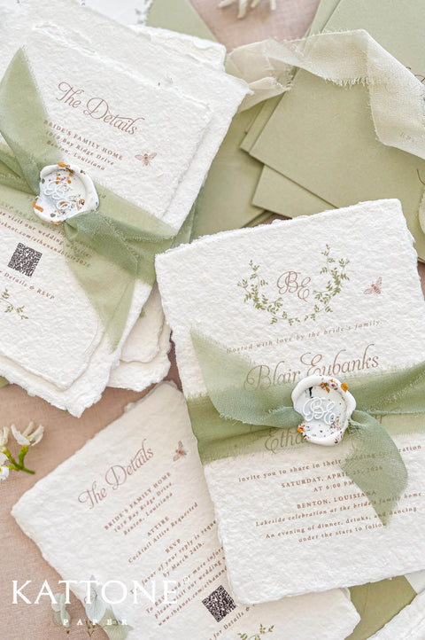 Hand-torn sage green silk ribbon wrapped around handmade wedding invitation secured with decorative wax seal.