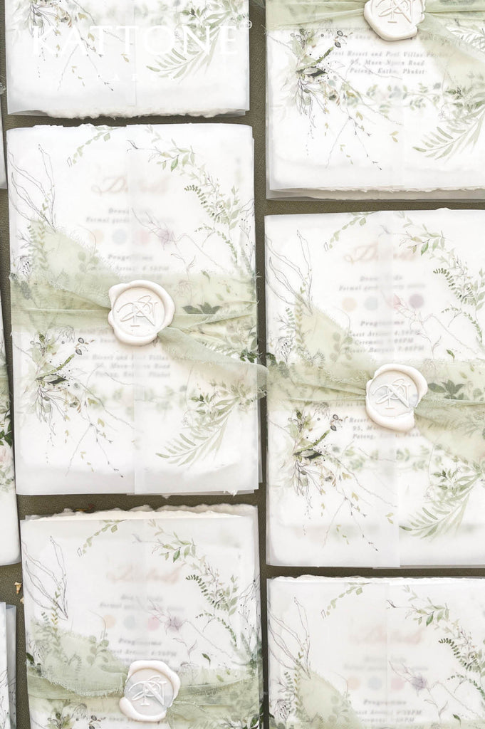 Stacked handmade paper botanical wedding invitations showcasing deckle edges and fine-art paper texture.