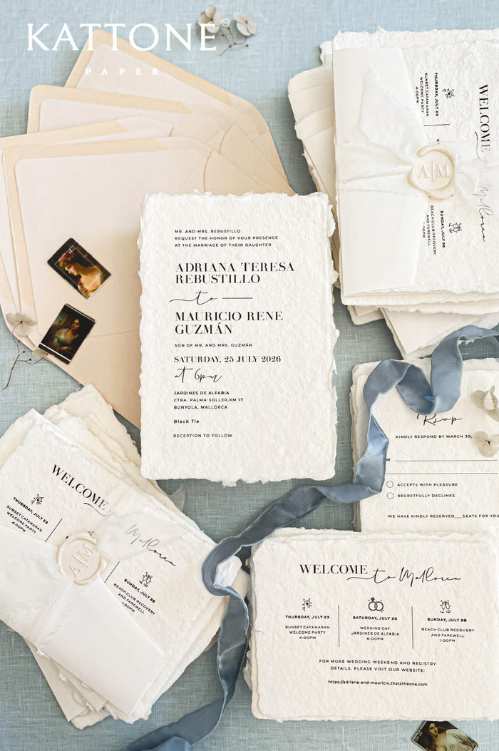 Luxury handmade cotton paper wedding invitation with deckled edges and modern typography, styled with silk ribbon, wax seal, beige envelopes and full coordinated stationery suite on soft blue background.