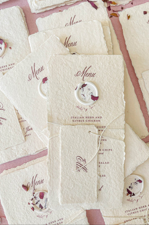 Handmade paper wedding menu with deckled edges, wax seal detail, personalized name tag, fine art reception stationery flat lay.