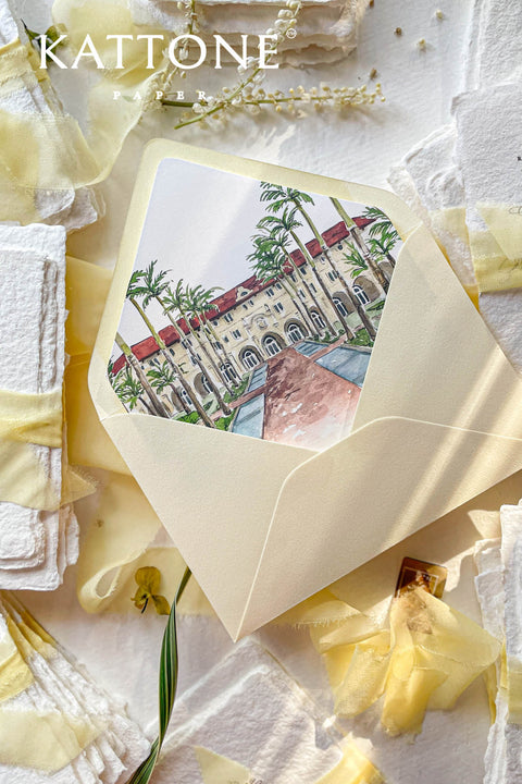 Soft yellow wedding envelopes with watercolor venue envelope liners styled with handmade paper, silk ribbon, and fine art stationery details.