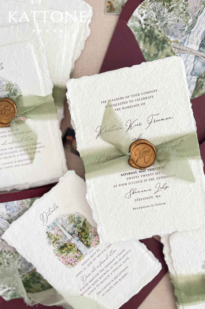 Fine art wedding invitation suite styled with handmade paper invitations, sage ribbon, burgundy envelopes and watercolor landscape artwork.