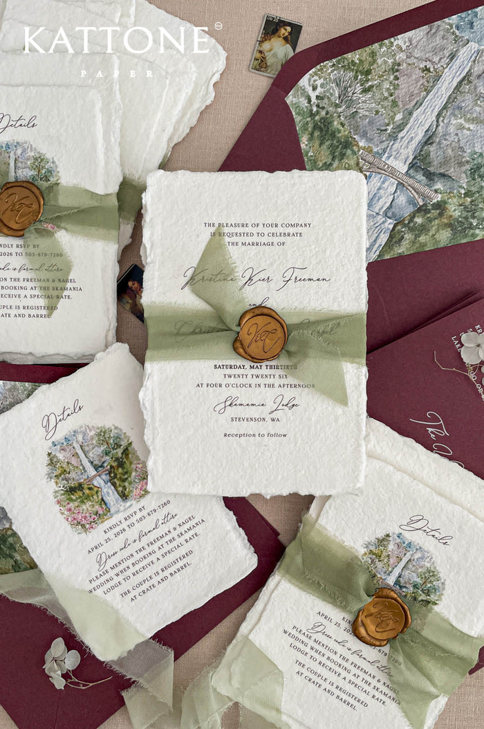 Luxury handmade cotton paper wedding invitation with deckled edges wrapped in sage silk ribbon and wax seal, styled with burgundy envelopes and scenic watercolor artwork cards.