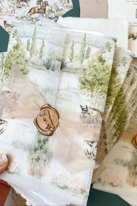 Wedding invitation wrapped in translucent vellum overlay revealing custom watercolor artwork on embossed handmade paper.