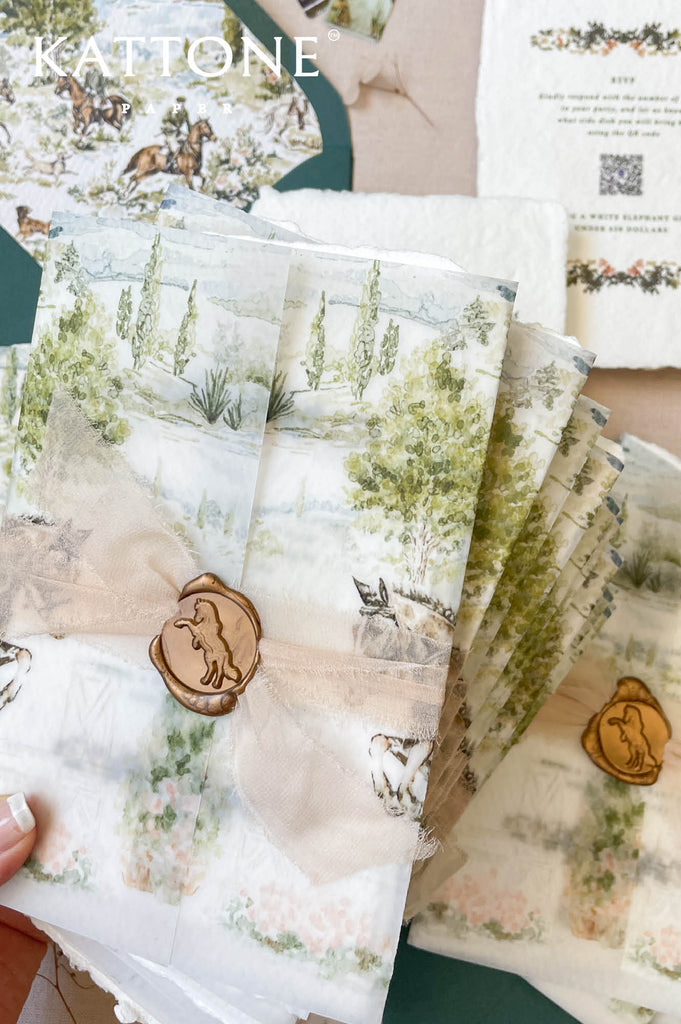 Wedding invitation wrapped in translucent vellum overlay revealing custom watercolor artwork on embossed handmade paper.