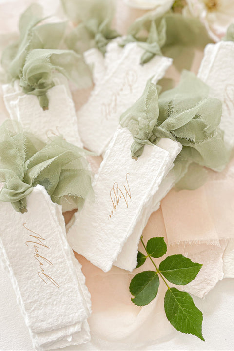 Bring soft, romantic elegance to your event with our handmade paper place cards, crafted from luxurious cotton rag paper and finished with natural deckled edges. Each card is adorned with airy sage-green chiffon ribbon and delicate calligraphy, creating a refined fine-art look perfect for weddings, showers, garden celebrations, and intimate gatherings. These artisanal place cards add movement, texture, and timeless beauty to any tablescape.