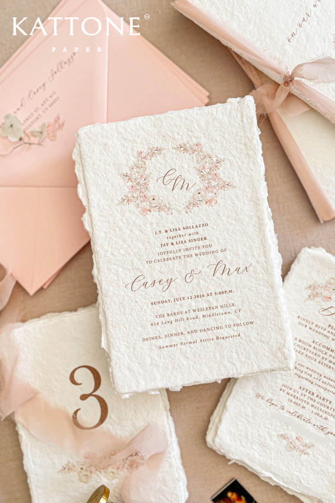Close up of textured handmade cotton paper invitation highlighting deckled edges, delicate watercolor floral wreath and soft script typography.