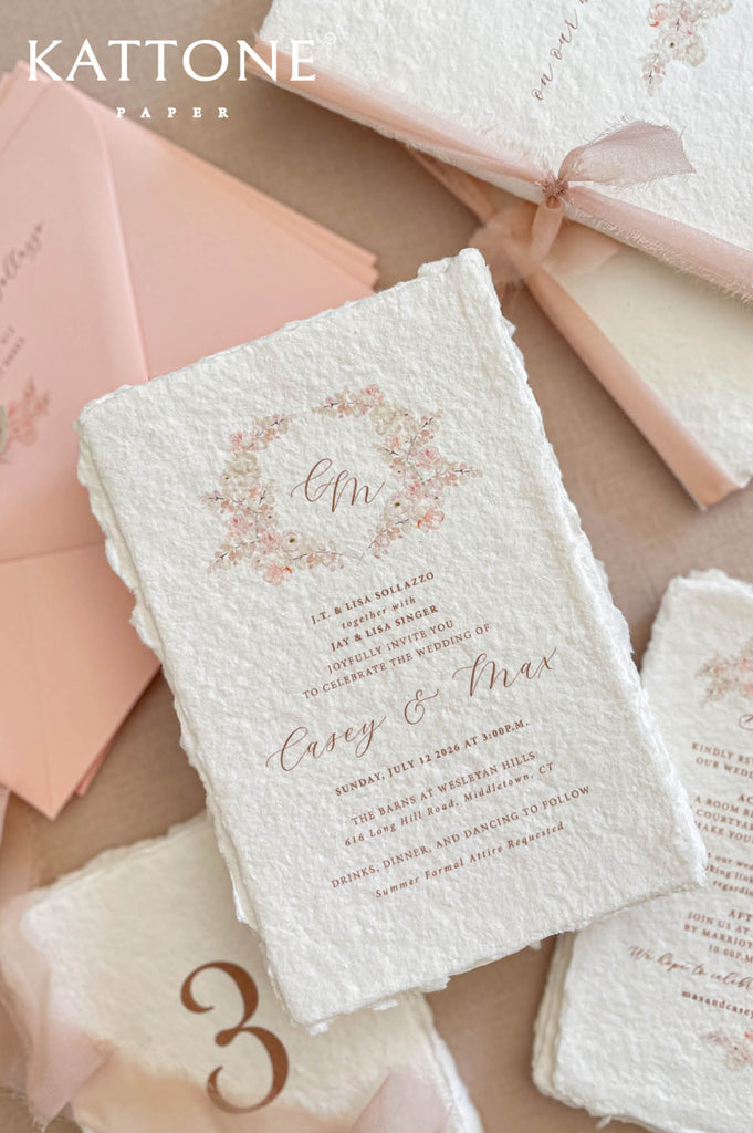 Close up of textured handmade cotton paper invitation highlighting deckled edges, delicate watercolor floral wreath and soft script typography.