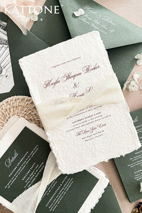 Romantic flat lay of luxury wedding stationery showcasing handmade paper invitations, deep green envelopes, venue artwork, and coordinating inserts.