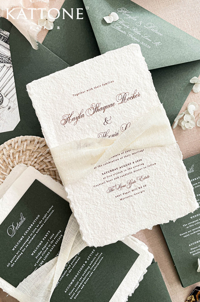 Romantic flat lay of luxury wedding stationery showcasing handmade paper invitations, deep green envelopes, venue artwork, and coordinating inserts.