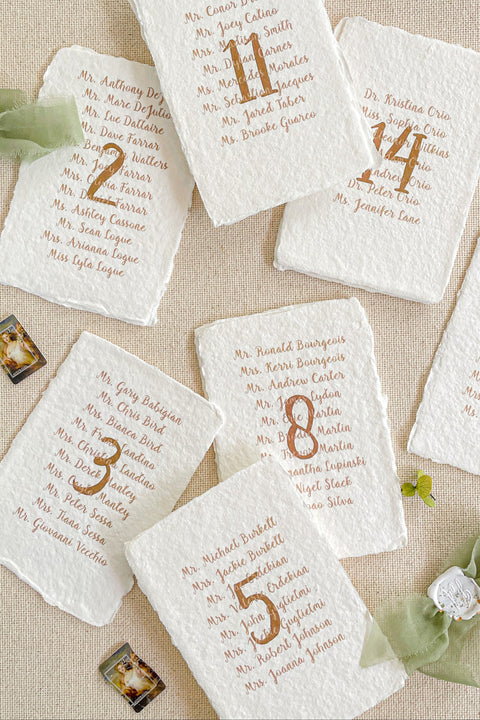 Handmade cotton paper paired with warm gold typography creates a refined and personalized table number design that elevates your seating presentation. Each card features a striking gold numeral centered above a beautifully arranged guest list, offering both elegance and functionality. The natural deckle edges and soft paper texture add an organic, fine-art feel - perfect for classic, luxurious, and romantic wedding aesthetics.