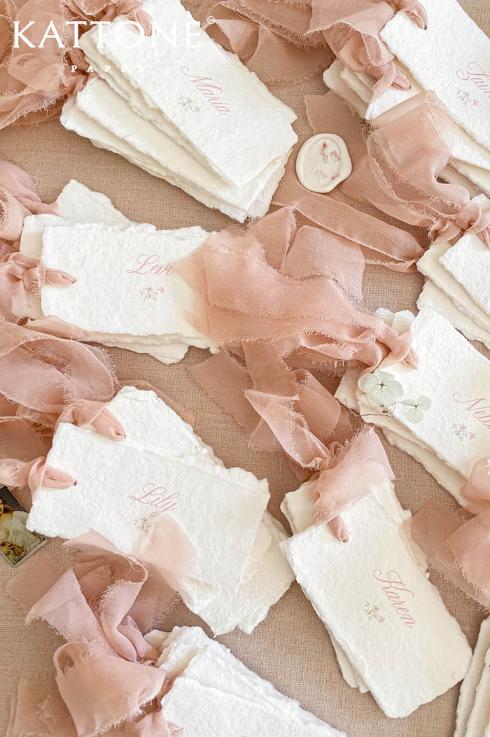 Handmade wedding place cards with deckled edges, soft blush silk ribbon and elegant script names on cotton paper.