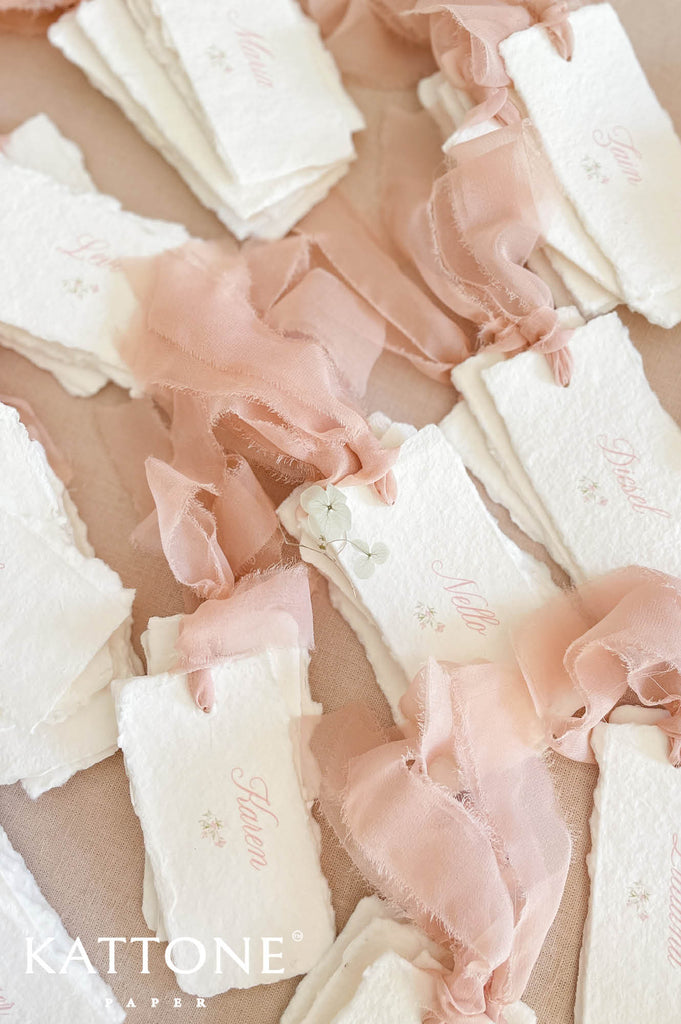 Close up of handmade cotton paper place card showing textured surface, deckled edges and flowing chiffon ribbon.
