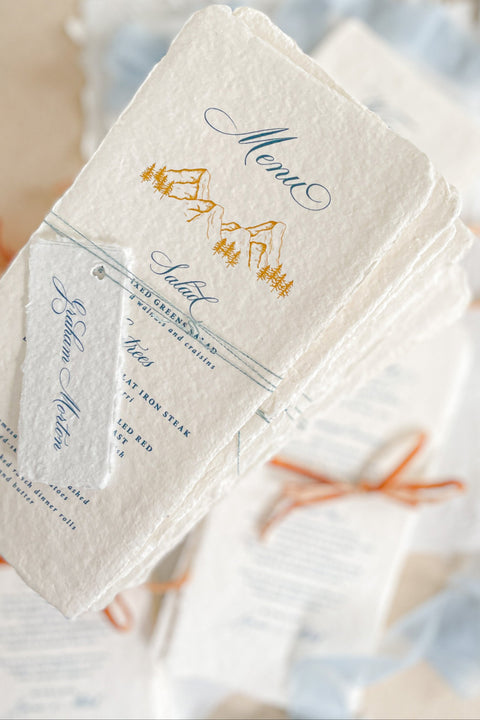 Capture timeless mountain charm with our handmade paper wedding menus, featuring soft deckled edges, textured cotton paper, and elegant alpine illustrations. Each piece is hand-pressed with artisanal care, pairing nature-inspired design with fine typography for an effortlessly elevated tablescape. Perfect for destination, outdoor, or rustic-elegant weddings, these menus bring natural sophistication to every detail.