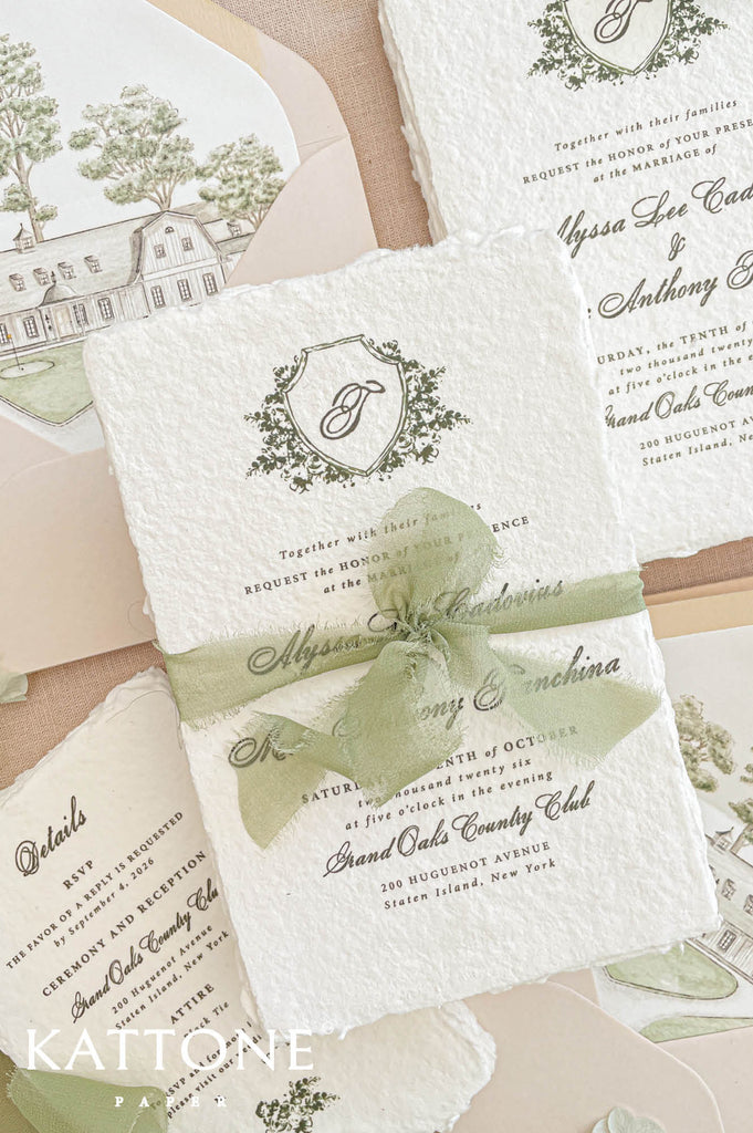 Elegant deckled edge handmade cotton paper wedding invitation with botanical crest monogram, refined script typography, and soft sage chiffon ribbon wrap, designed in a romantic blush and green color palette.