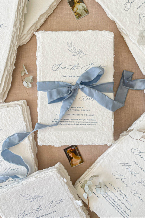 Handmade save the date card with deckled edge cotton paper, soft blue silk ribbon bow and elegant calligraphy typography in fine art wedding stationery style.