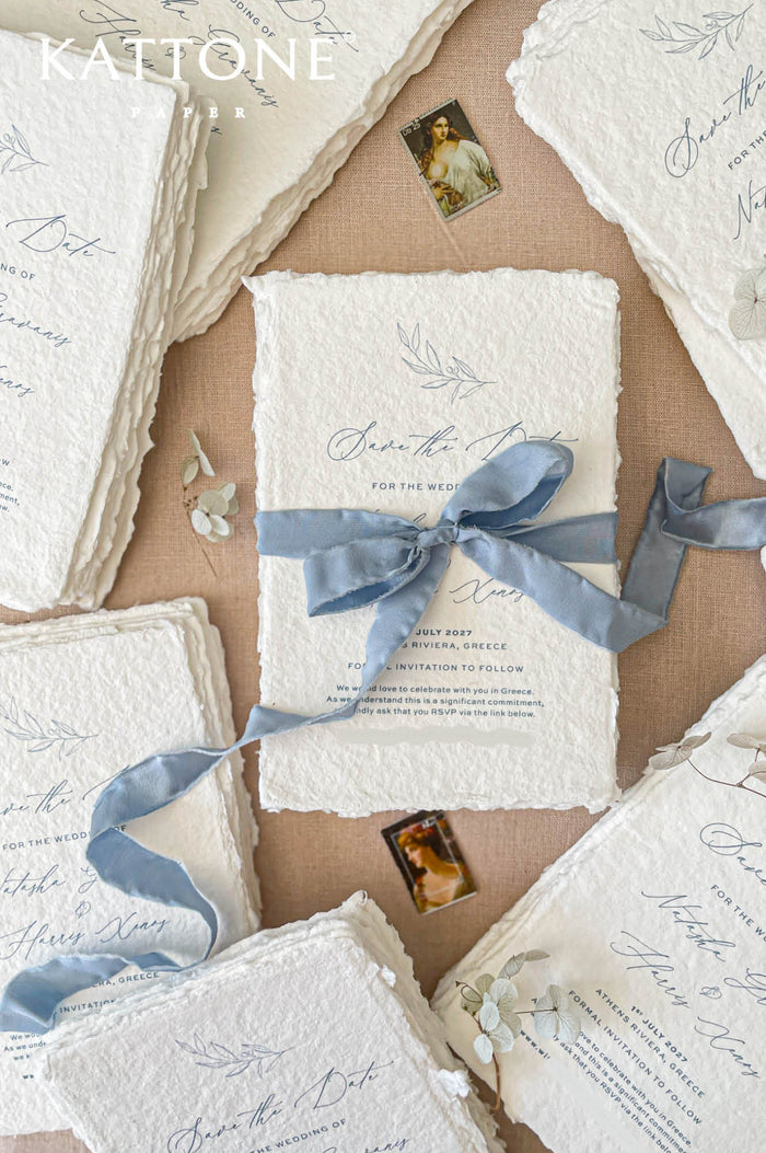 Handmade save the date card with deckled edge cotton paper, soft blue silk ribbon bow and elegant calligraphy typography in fine art wedding stationery style.