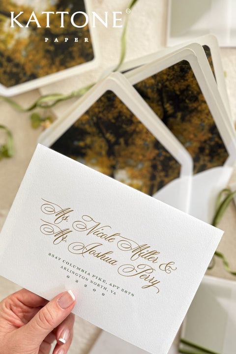 White wedding envelopes with address printing and envelope liners held in hand, showcasing elegant typography and layered fine art stationery styling.