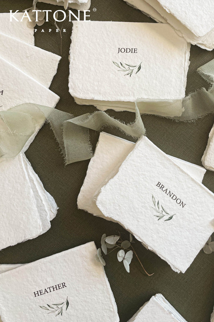 Handmade wedding place cards with deckled edges, botanical greenery illustration and elegant serif names on cotton paper.