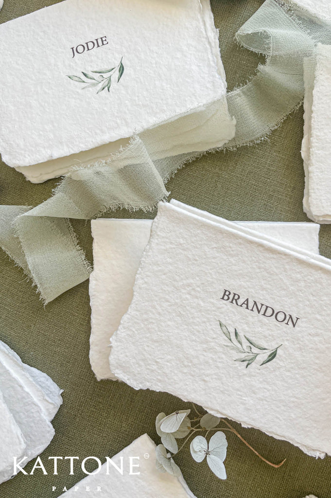 Close up of cotton paper place card showing textured surface, deckled edges and delicate leaf illustration.