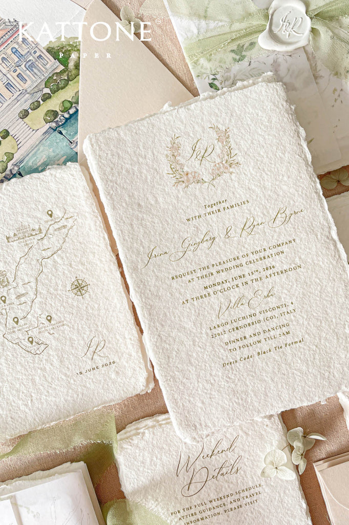 Romantic flat lay of luxury wedding stationery showcasing handmade paper invitations, vellum wraps, watercolor venue artwork, map cards, wax seals, chiffon ribbon, and coordinating envelopes.