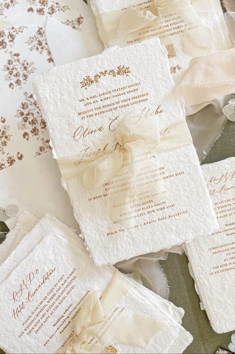 Close up of handmade cotton paper invitation showing textured deckled edges, soft floral motifs and elegant typography in warm neutral tones.