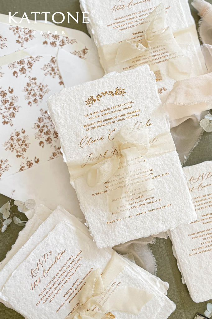 Close up of handmade cotton paper invitation showing textured deckled edges, soft floral motifs and elegant typography in warm neutral tones.