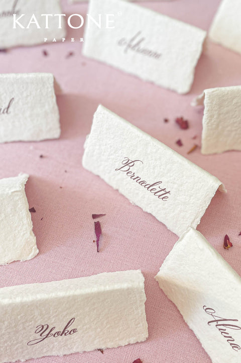 Close-up of handmade cotton paper place card featuring elegant calligraphy guest name and natural deckled edges.