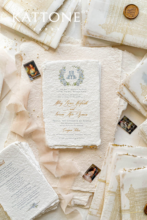 This handmade paper wedding invitation suite combines fine craftsmanship with opulent detailing. Printed on luxury cotton paper with deckled edges, each invitation is accented with subtle touches of gold leaf, catching the light with a refined shimmer that speaks of romance and sophistication. The design features a hand-painted floral monogram, symbolizing the couple’s union, surrounded by soft watercolor greenery and pastel hues.