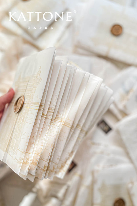 This handmade paper wedding invitation suite combines fine craftsmanship with opulent detailing. Printed on luxury cotton paper with deckled edges, each invitation is accented with subtle touches of gold leaf, catching the light with a refined shimmer that speaks of romance and sophistication. The design features a hand-painted floral monogram, symbolizing the couple’s union, surrounded by soft watercolor greenery and pastel hues.