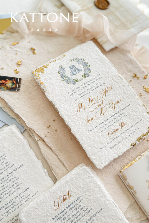 This handmade paper wedding invitation suite combines fine craftsmanship with opulent detailing. Printed on luxury cotton paper with deckled edges, each invitation is accented with subtle touches of gold leaf, catching the light with a refined shimmer that speaks of romance and sophistication. The design features a hand-painted floral monogram, symbolizing the couple’s union, surrounded by soft watercolor greenery and pastel hues.