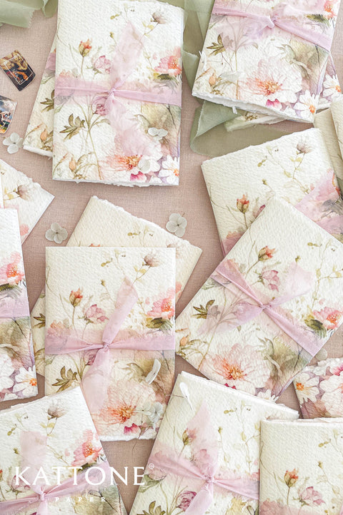 Soft translucent vellum wrap layered over tri-fold handmade paper wedding invitations, showcasing floral artwork beneath for an elevated presentation.
